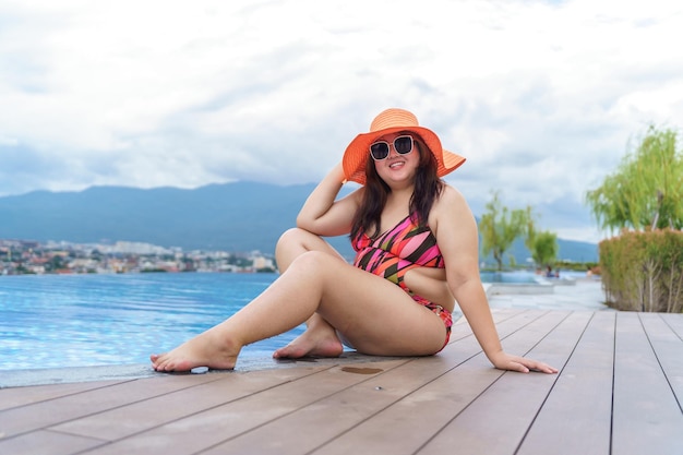 Overgewicht jonge aziatische vrouw draagt oranje zwempak en stro strand zonnehoed ontspannen in zwembad Gelukkig plus size vrouw vrolijk grappig vakantie reizen in de zomer