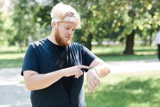 Overgewicht man met fitness tracker op zijn hand tijdens het joggen in het park buiten