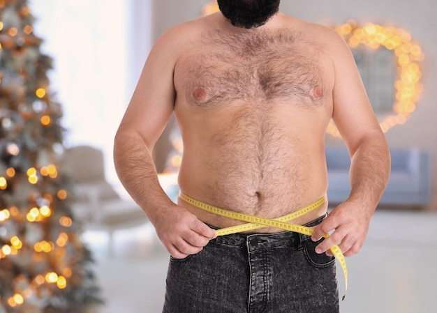 Overgewicht man zijn taille meten in de kamer met kerstboom na vakantie close-up