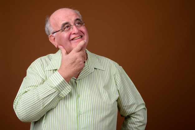 Overgewicht senior man met bril tegen bruine muur