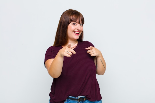 Overgewicht vrouw lachend met een positieve, succesvolle, gelukkige houding wijzend naar de camera, pistool teken met handen maken