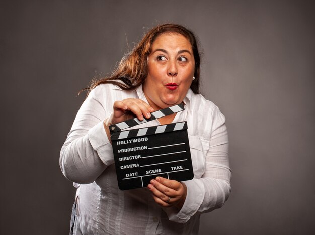 Overgewicht vrouw met een film klepel bord op een grijze achtergrond