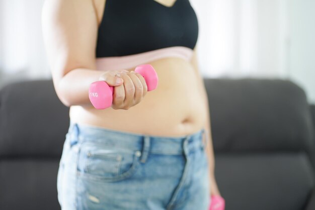 Overgewicht vrouw trainen voor gewichtsverlies oefening met halters in stretch posities thuis in de woonkamer Vrolijke dikke vrouw dieet gezonde levensstijl concept