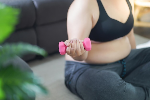 Overgewicht vrouw trainen voor gewichtsverlies oefening met halters in stretch posities thuis in de woonkamer Vrolijke dikke vrouw dieet gezonde levensstijl concept