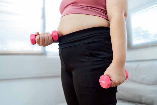 Overgewicht vrouw trainen voor gewichtsverlies oefening met halters in stretch posities thuis in de woonkamer Vrolijke dikke vrouw dieet gezonde levensstijl
