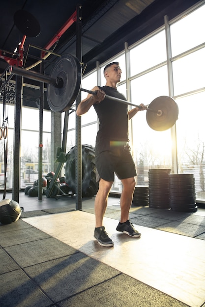 Photo overgoing. young muscular caucasian athlete training in gym, doing strength exercises, practicing, work on his upper body with weights and barbell. fitness, wellness, healthy lifestyle concept.