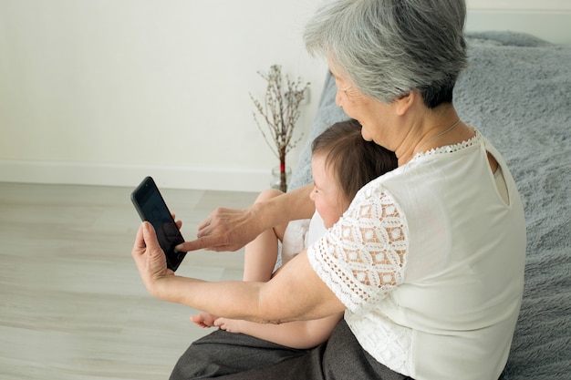 Overgrootmoeder zit met achterkleindochter en kijkt in de smartphone.