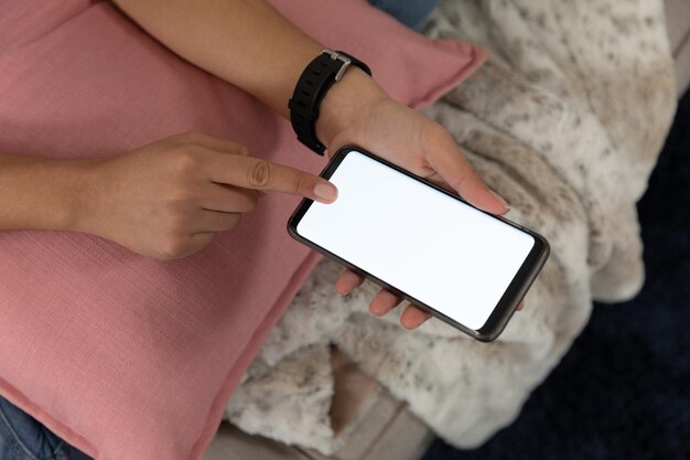 Фото Крупный план рук молодой белой женщины, использующей сенсорный экран смартфона, сидящей на диване в своей гостиной.
