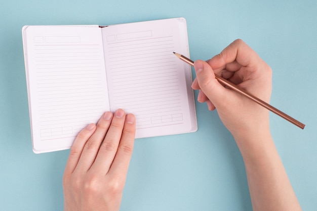 Overhead above close up view photo of female girl hands holding pencil starting to do homework in copy book isolated over pastel color blue background