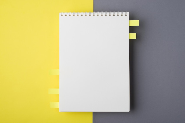 Над головой над крупным планом плоская планировка фото открытого чистого учебника по дизайну с памятными бумагами, изолированными наполовину серым и ярко-желтым столом