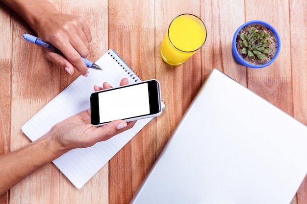 Photo overhead of feminine hands holding smartphone and taking notes