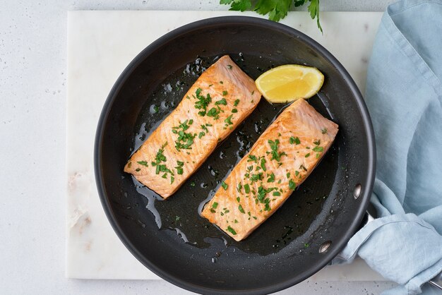 Overhead of fried juicy salmon fillet with parsley and lemon on frypan