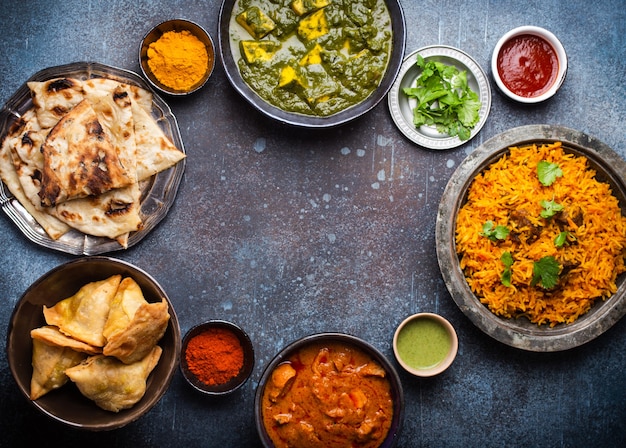 Overhead of Indian traditional dishes and appetizers: chicken curry, pilaf, naan bread, samosas, paneer, chutney on rustic background. Table with choice of food of Indian cuisine, space for text