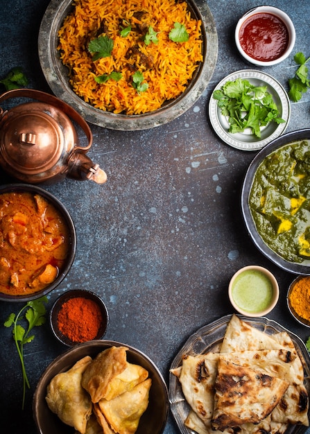 Overhead of Indian traditional dishes and appetizers: chicken curry, pilaf, naan bread, samosas, paneer, chutney on rustic background. Table with choice of food of Indian cuisine, space for text