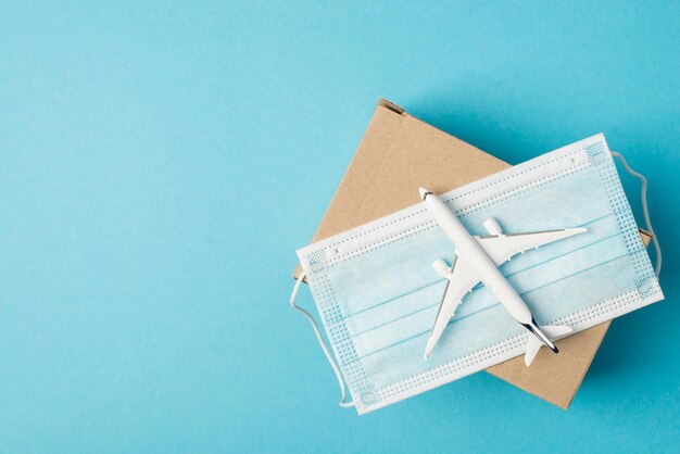 Overhead photo of airplane and box humanitarian aid donation with face mask isolated on the blue background with copyspace