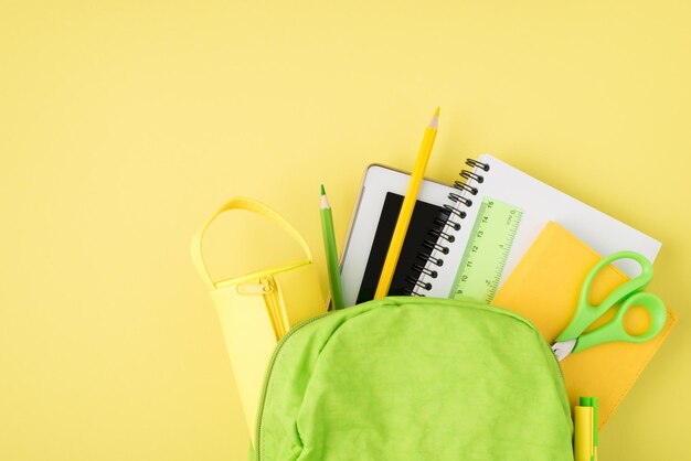 노란색 배경에 격리된 배낭 눈금자 메모장 펜 연필 태블릿 및 연필 케이스의 머리 위 사진