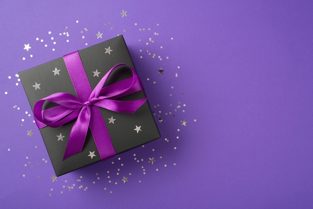 Photo overhead photo of black giftbox with ribbon wrapped as bow and confetti around isolated on the violet background