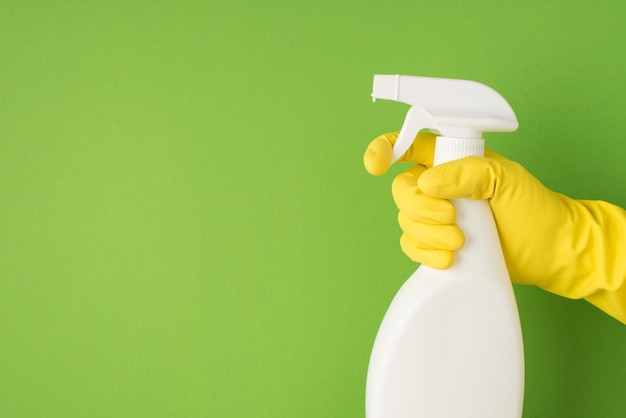 Overhead photo of cleaning spray and hands in yellow gloves isolated on the green background