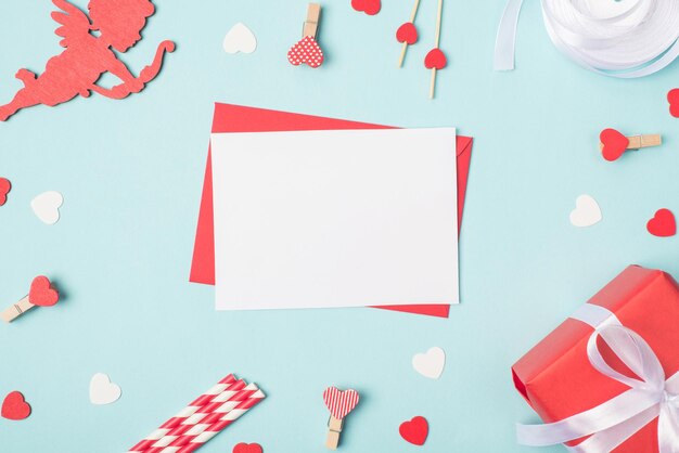 Overhead photo of empty sheet of paper with place for mock up on blue table with amour cupid pins hearts and giftbox