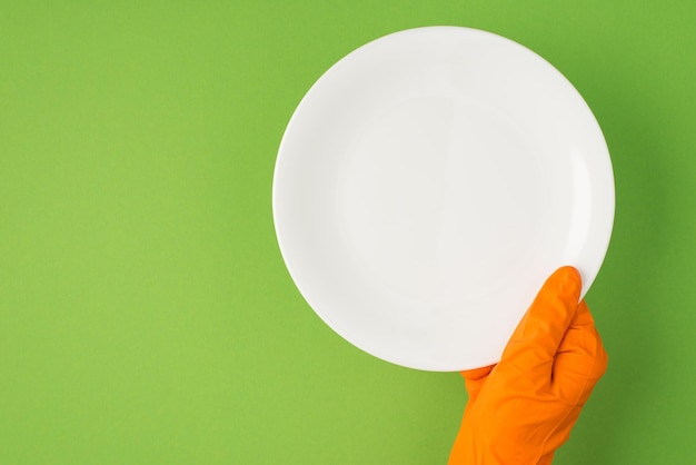 Overhead photo of hands in orange gloves holding a dish isolated on the green background