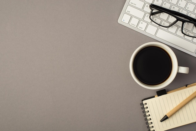 Foto dall'alto della tastiera con penna occhiali tazza di caffè e taccuino isolato su sfondo grigio con copyspace