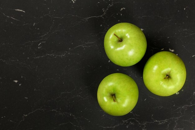 Overhead schot - drie groene appels op een zwart bord, ruimte voor tekst aan de linkerkant.