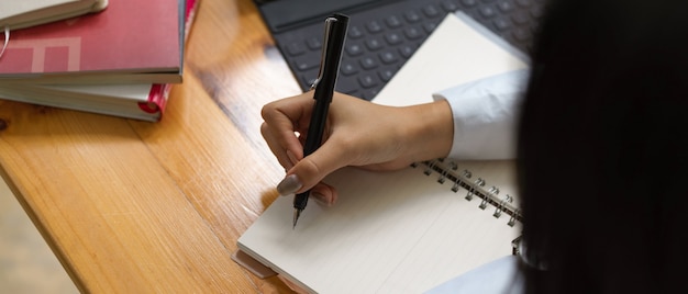 Overhead schot van vrouwelijke schrijven op lege notebook met leveringen op houten tafel