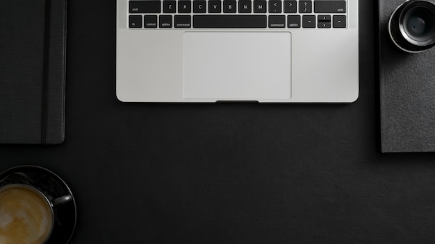 Photo overhead shot of dark modern workspace with laptop, coffee cup and office supplies