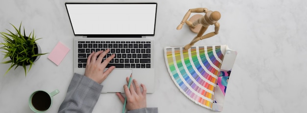 Overhead shot of designer working on mock-up laptop and designer supplies on marble table