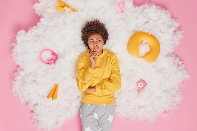 Overhead shot of displeased Afro American woman dressed in pajama thinks deeply about future