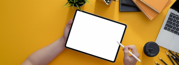 Overhead shot of freelancer writing on blank screen tablet with stylus on yellow worktable