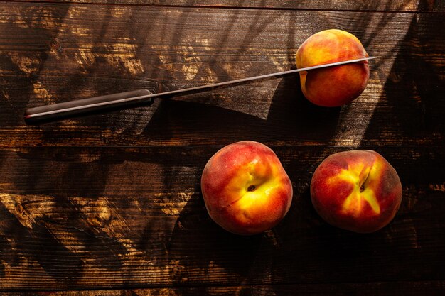 Снимок свежих спелых сезонных персиков сверху и нож на деревянном столе