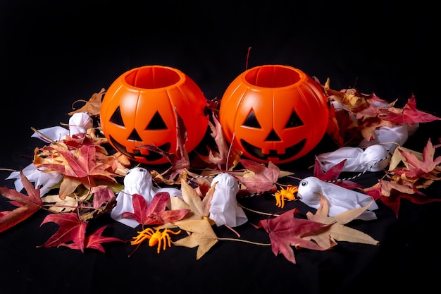 Overhead shot of Halloween pumpkins over red autumn leaves and ghosts on a black background