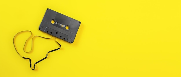 Overhead shot - magnetic audio cassette with some tape out, on yellow board, wide banner space for text on right side