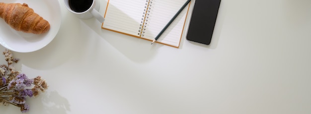 Overhead shot of minimal worktable with open blank notebook, smartphone, breakfast meal and copy space