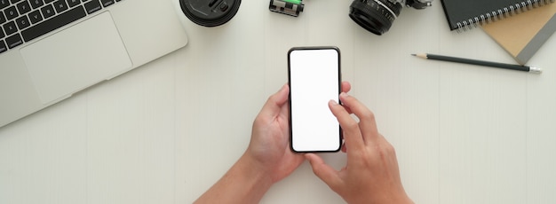 白い作業台でモックアップのスマートフォンを使用して写真家の俯瞰写真
