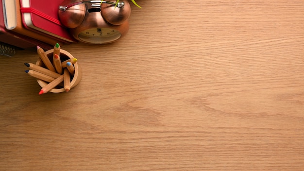 Overhead shot of simple workspace with colour pencils clock books and copy space on wooden table