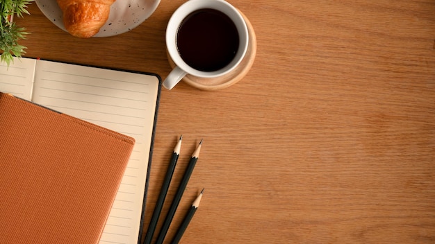 ノートブック、鉛筆、コーヒー、木製の背景にコピースペースと学習テーブルのオーバーヘッドショット。