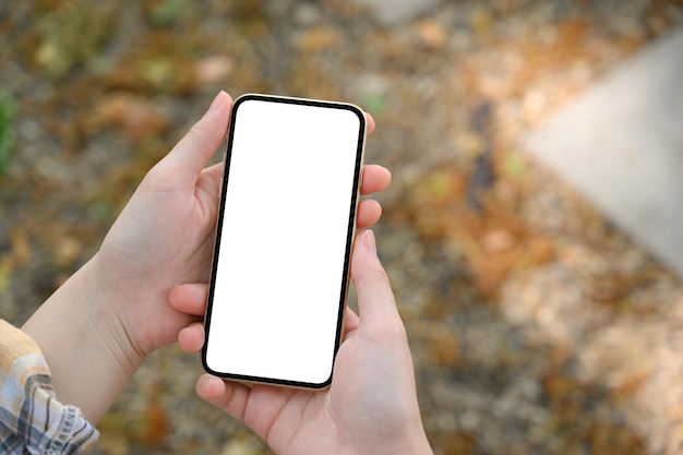 Overhead shot Vrouwelijke handen met een mockup met een leeg scherm van een smartphone over een wazige straatachtergrond