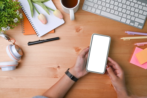 Overhead shot of woman holding smart phone on wooden desk.