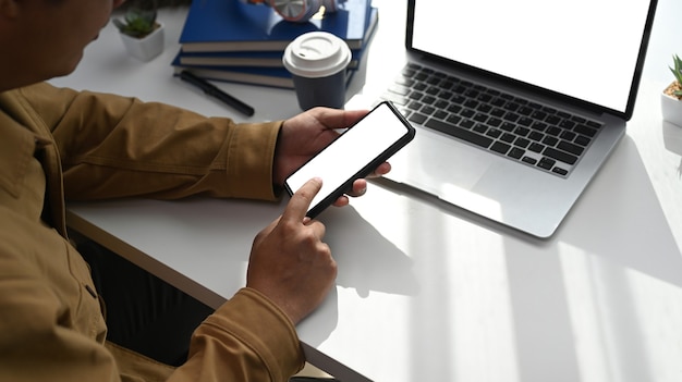 Overhead shot of young man sitting in front of laptop and using smart phone at home office.