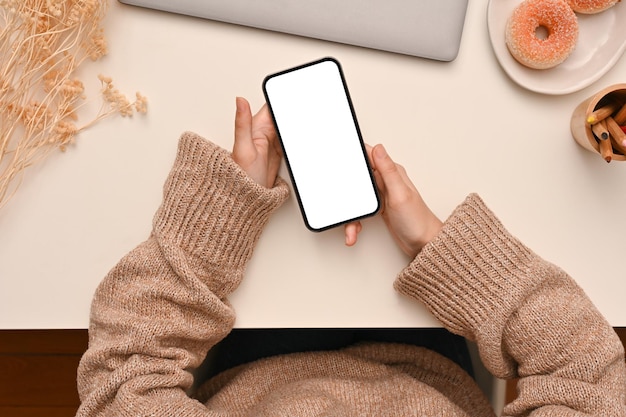 Overhead van een vrouw in een comfortabele trui met een moderne mobiele telefoon op haar bureau