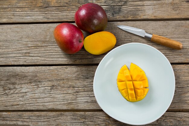 Foto overhead van gehalveerde en gehakte mango's met mes op houten tafel