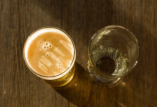 Foto overhead van glas bier naast leeg glas op houten tafel