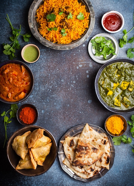 Overhead van Indiase traditionele gerechten en hapjes: kip curry, pilaf, naan brood, samosa's, paneer, chutney op rustieke achtergrond. Tafel met keuze aan gerechten uit de Indiase keuken, ruimte voor tekst