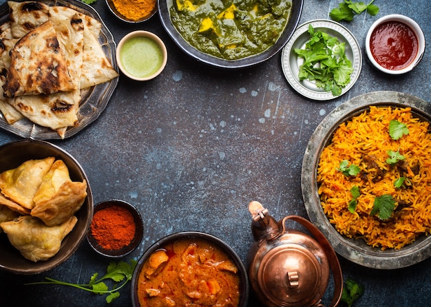 Overhead van Indiase traditionele gerechten en hapjes: kip curry, pilaf, naan brood, samosa's, paneer, chutney op rustieke achtergrond. Tafel met keuze aan gerechten uit de Indiase keuken, ruimte voor tekst