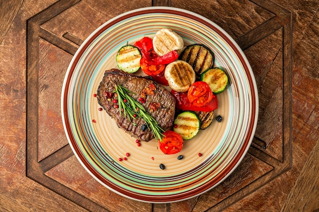 Overhead view of a beef steak with grilled vegetables garnish, zucchini, aubergine, mushroom, pepper, rosemary, cherry tomato