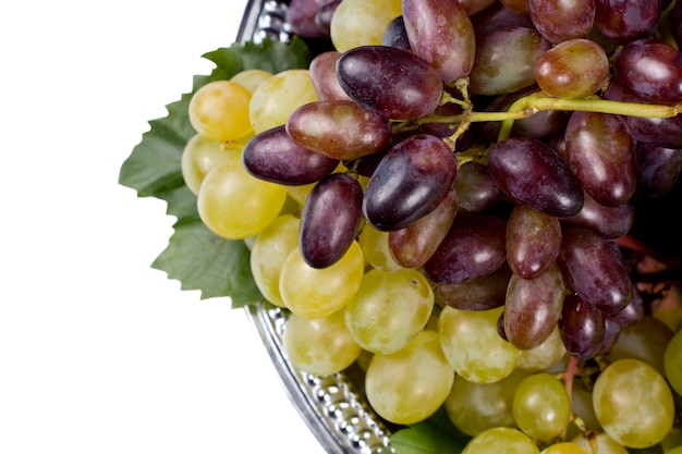 Overhead view of bunches of fresh red and green grapes on a metal tray, isolated on white