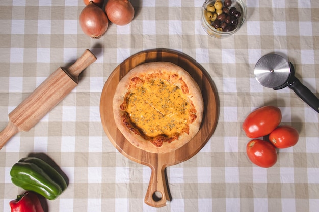 Overhead view of a cheddar pizza on top of a table with a checkered tablecloth