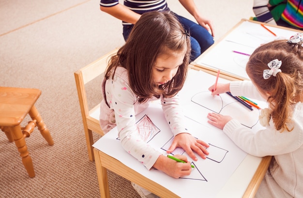 Overhead view of children in kindergarten learn letters and shapes coloring them